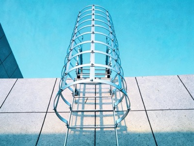 Échelle à crinoline à arceaux ronds présentée sur dalle béton, mur bleu en arrière-plan